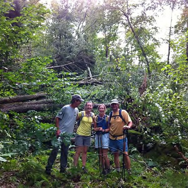 Photo of group of people in front of a pile of trees knocked down by a storm.
